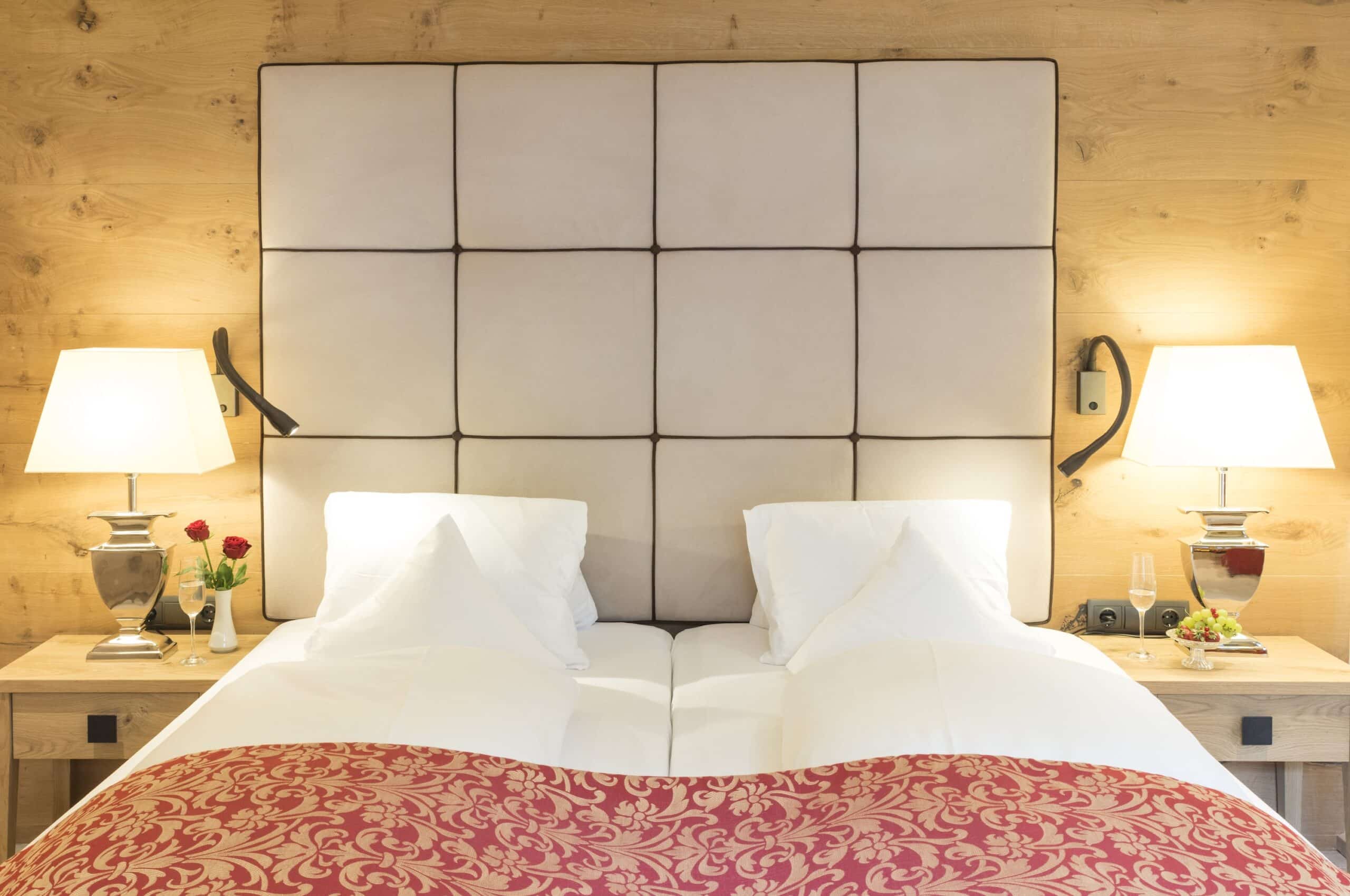 Gemütliches Hotelzimmer mit großem Bett, roter Bettdecke, gepolstertem Kopfteil und Holzwand im Hintergrund.