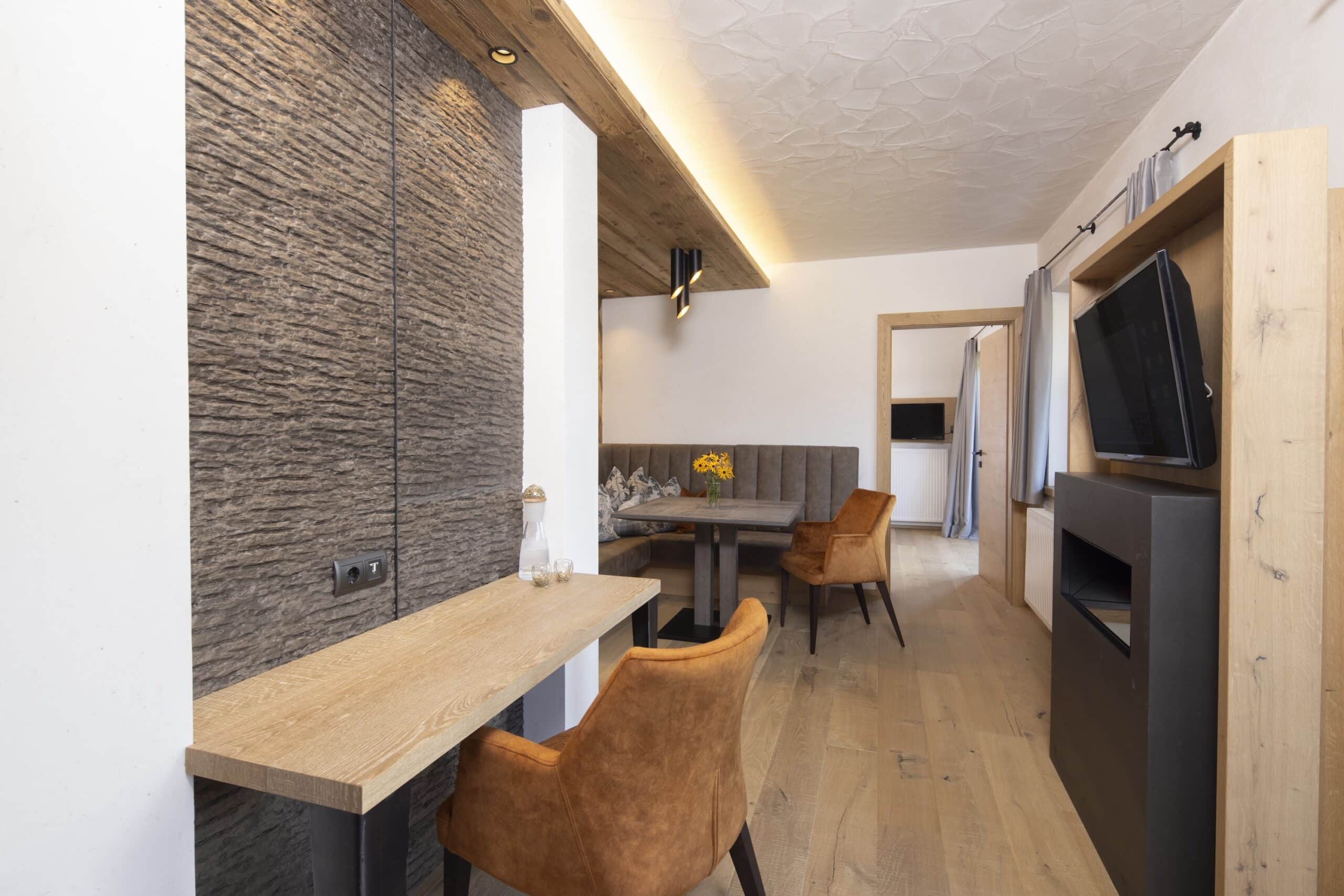 Modern eingerichtetes Wohnzimmer mit einer gemütlichen Sitzecke, Holztischen und einem Fernseher.
