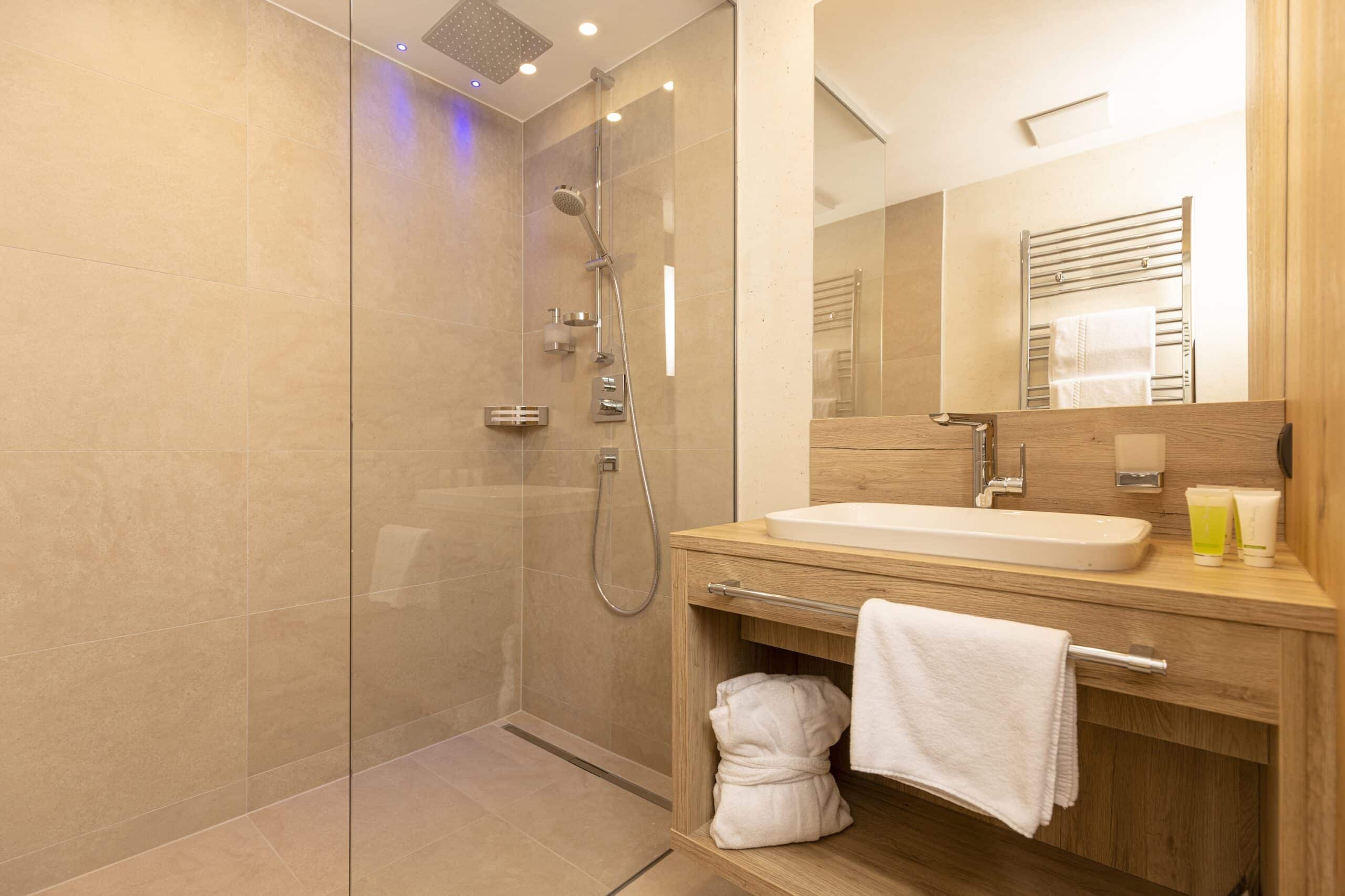 Moderne Badezimmerausstattung mit einer Glasduschkabine, einem Waschbecken auf einem Holzunterschrank und beige gefliesten Wänden.