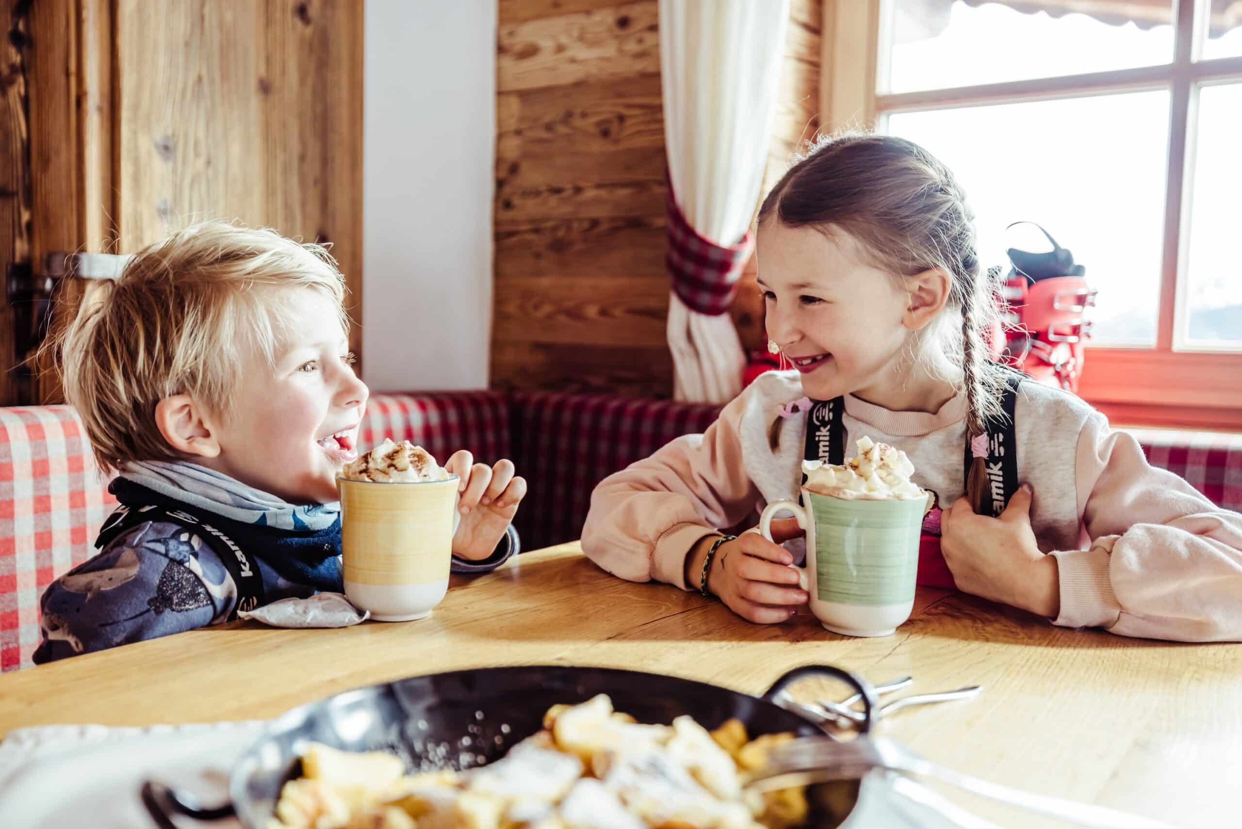 Kinder trinken Kakao in einer Alpenhütte an einem Teller Kaiserschmarren im Alpbachtal