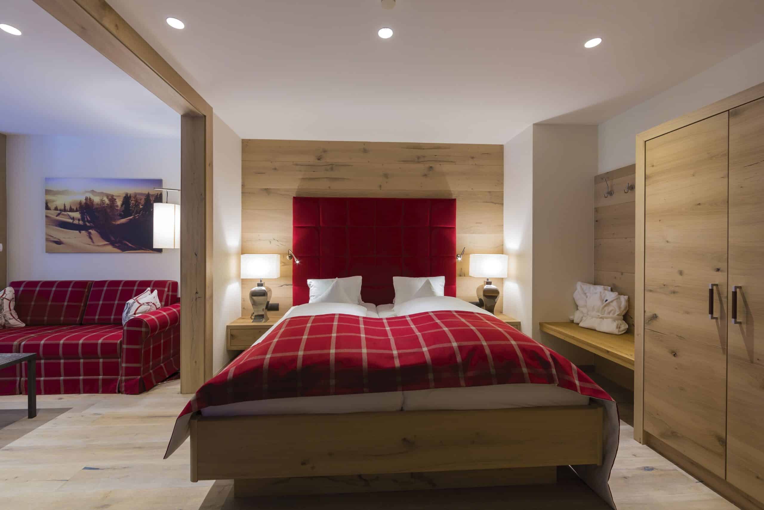 Gemütliches Schlafzimmer mit einem großen roten Bett, hölzernen Möbeln und einer sitzenden Leseecke.