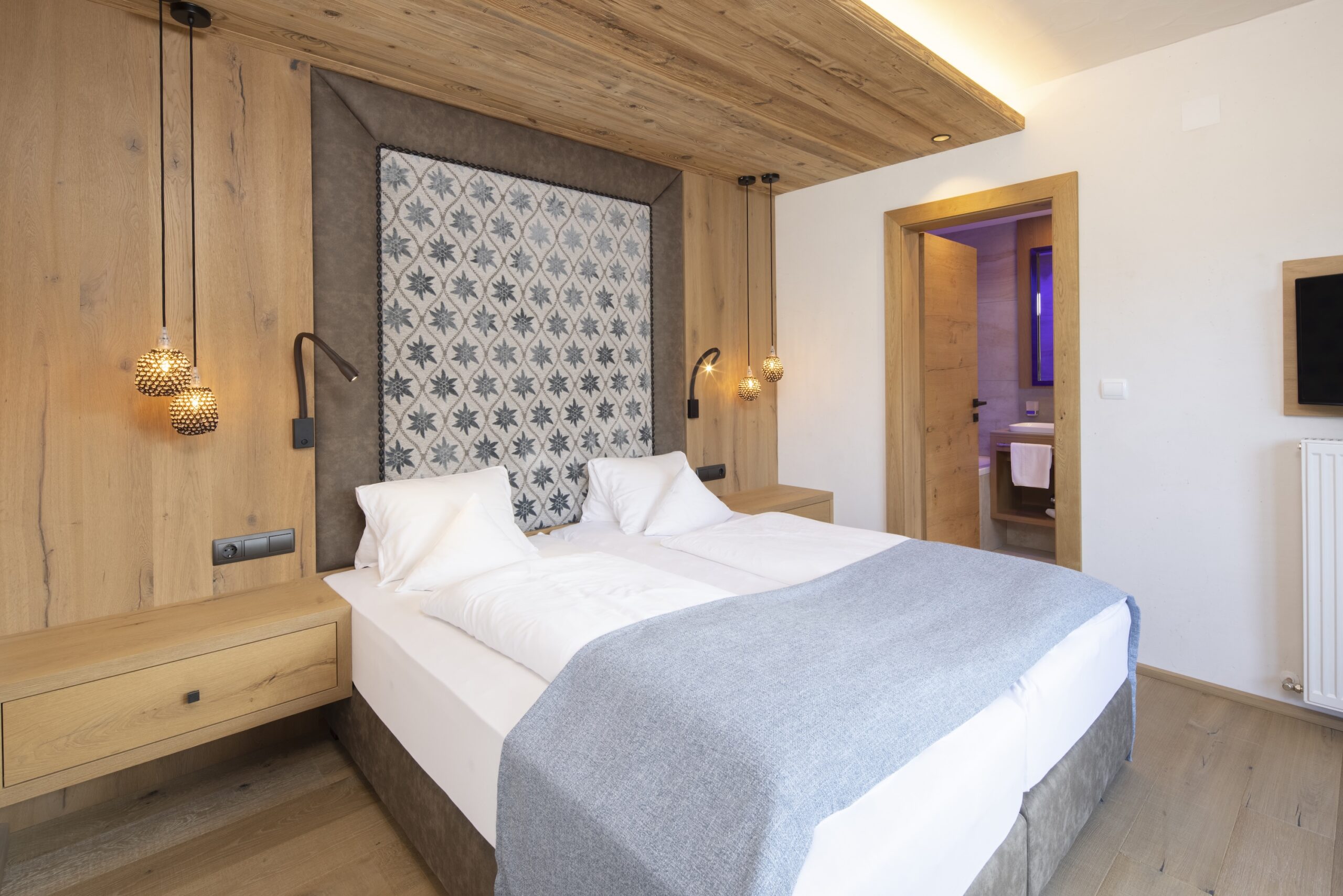 Modern eingerichtetes Schlafzimmer mit einem großen Doppelbett, hölzernen Wandpaneelen und stilvoller Beleuchtung.