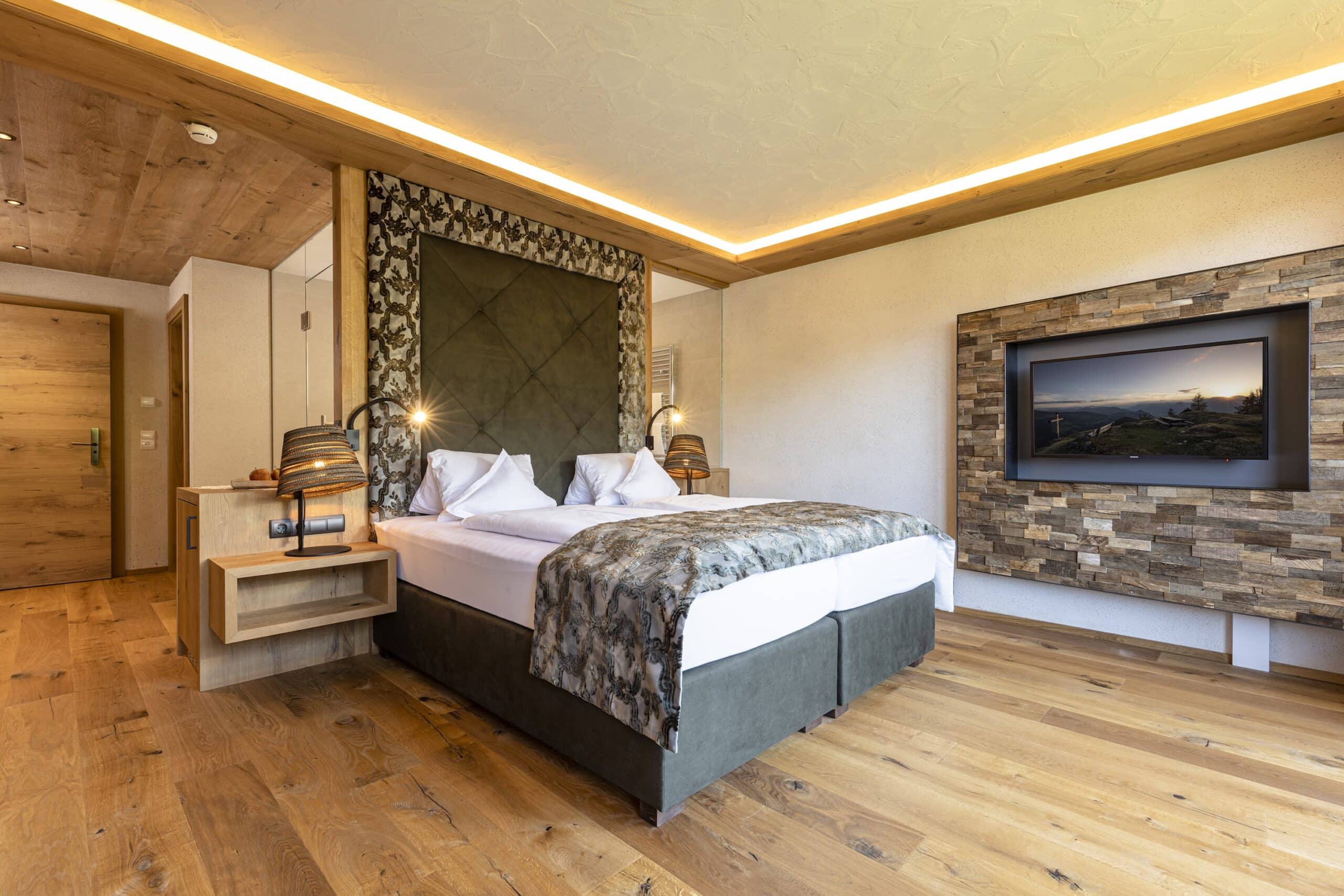 Modern eingerichtetes Schlafzimmer mit großem Doppelbett, hölzernen Wänden und einem Flachbildfernseher an der Wand.