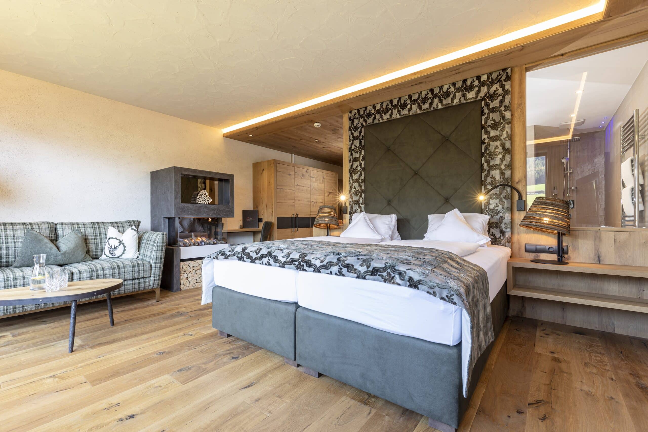 Luxuriöses Hotelzimmer mit großem Doppelbett, grünem Sofa, Holzboden und modernem Kamin.