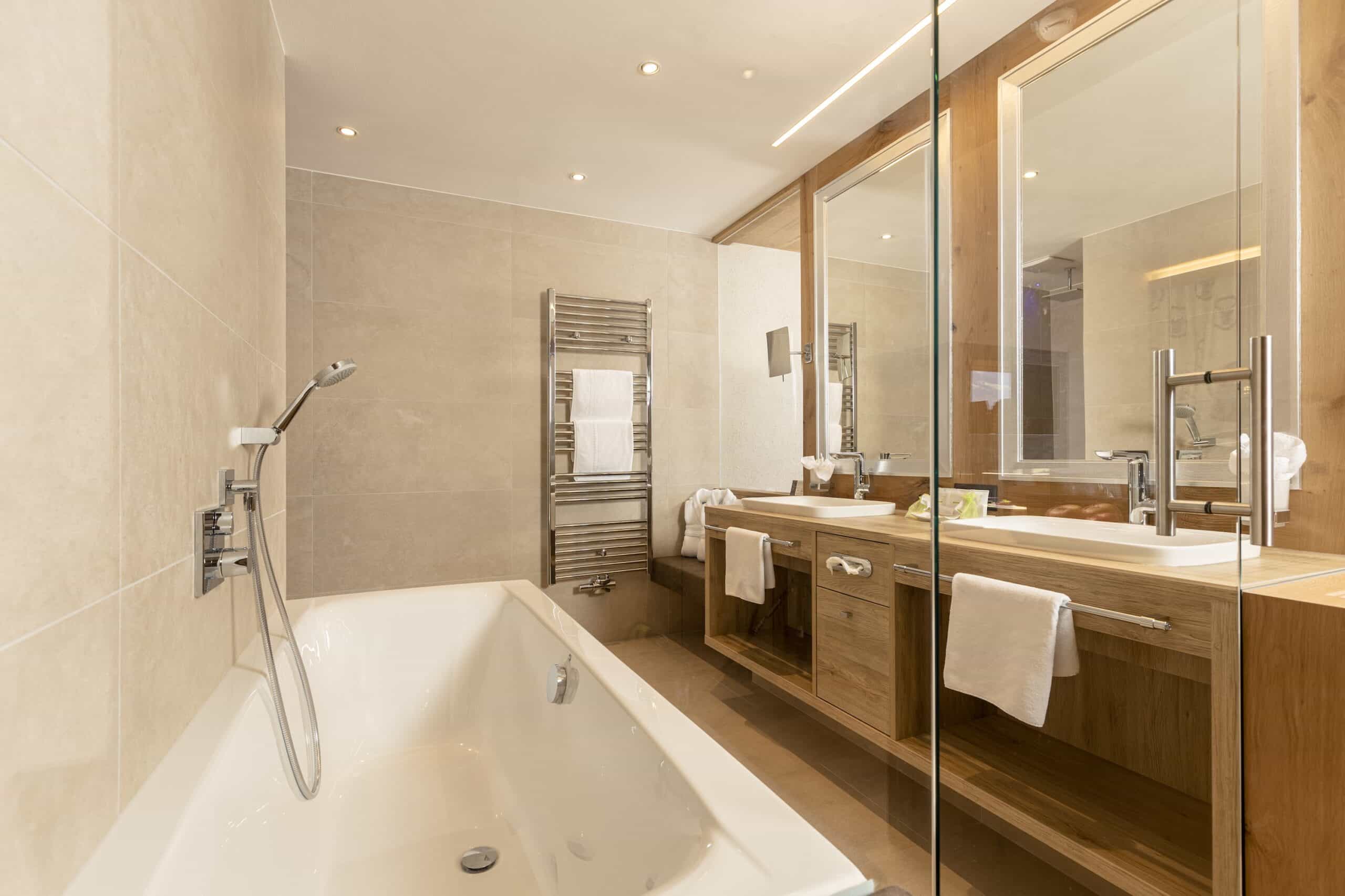 Modernes Badezimmer mit freistehender Badewanne, Holzschrank und großen Spiegeln.