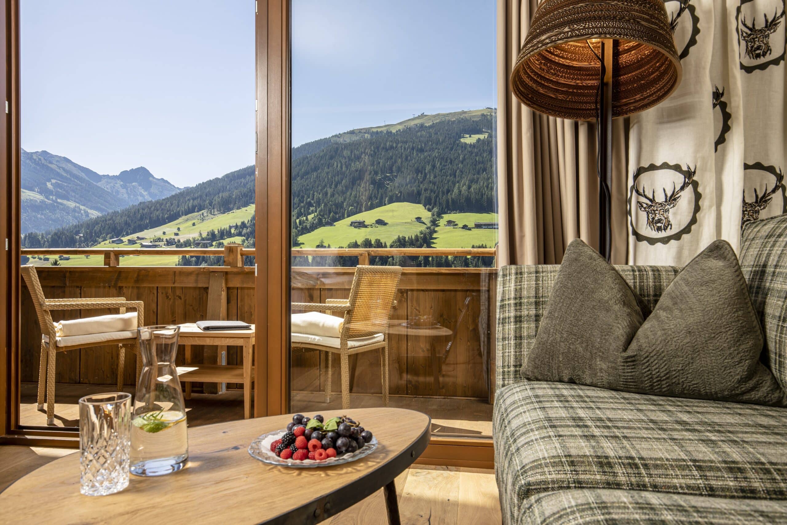 Gemütliche Sitzecke mit Sofa und Stühlen, mit Blick auf eine große Fensterfront, die eine malerische Aussicht auf ein Tal mit grünen Wiesen und Berge bietet.
