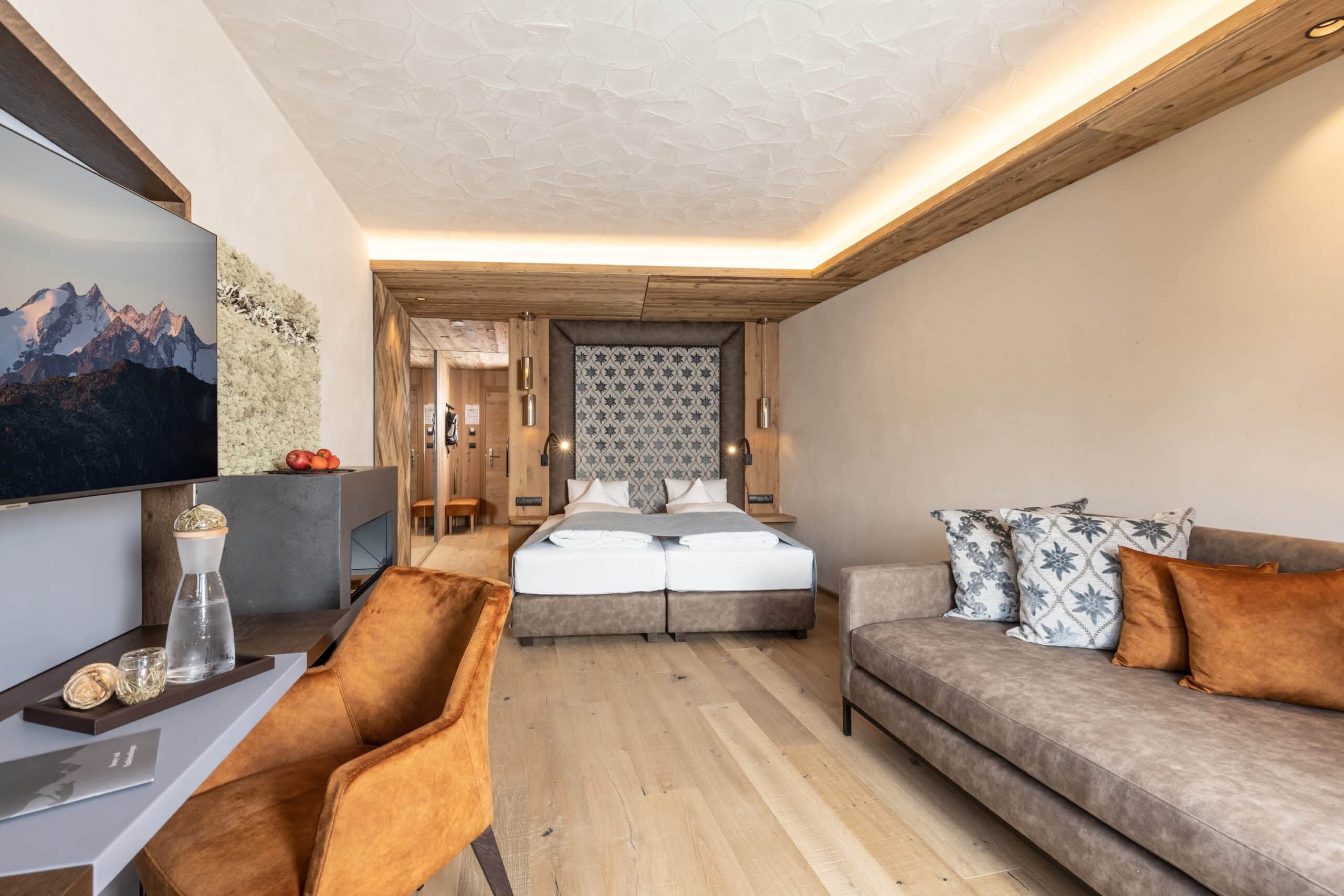 Ein stilvolles modernes Schlafzimmer mit einem Doppelbett, Sofa und Sesseln, Holzboden und einem großen Panoramafenster mit Blick auf die Berge.
