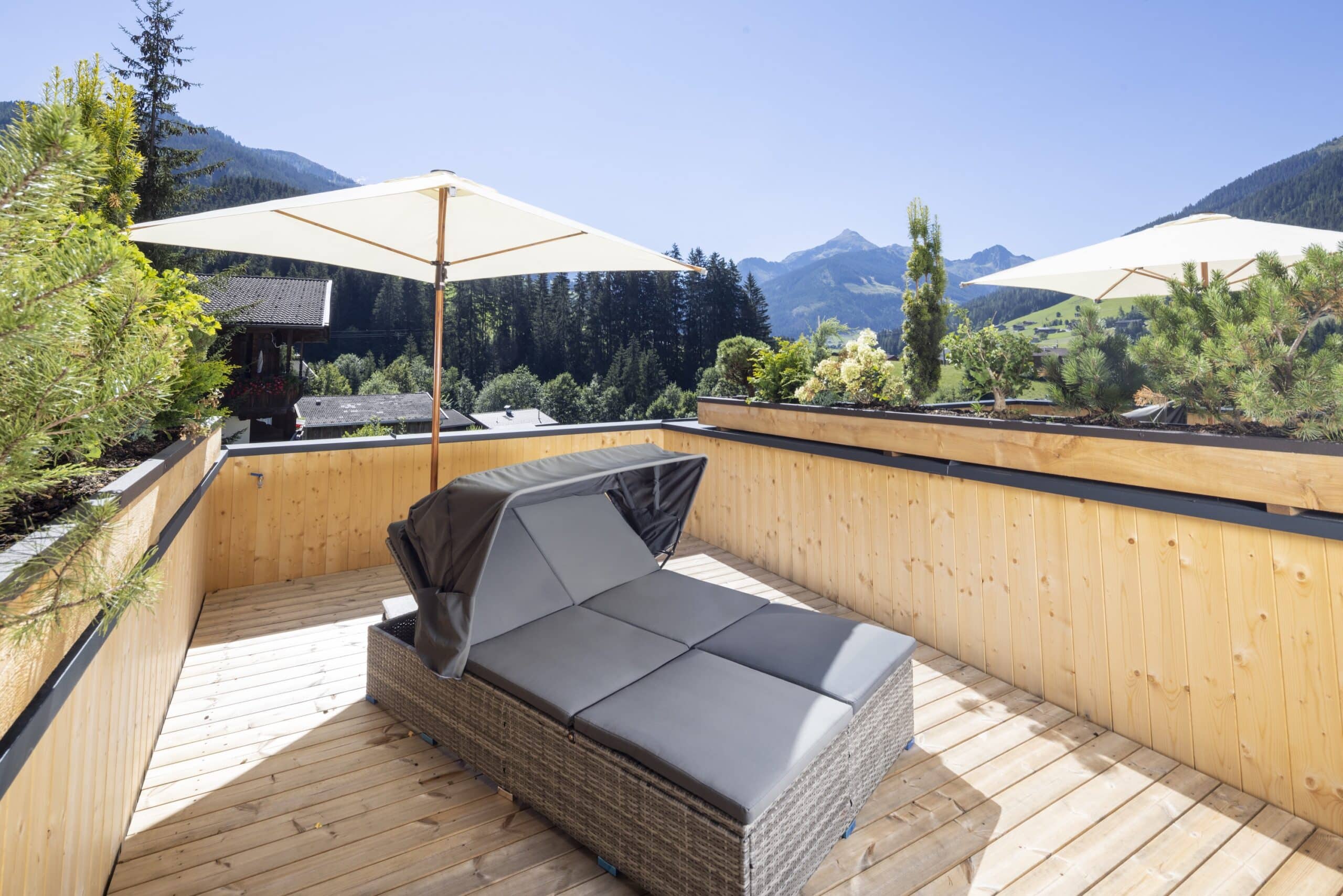 Holzterrasse mit modernem Lounge-Sofa und Sonnenschirmen mit Blick auf Berge und Wald.