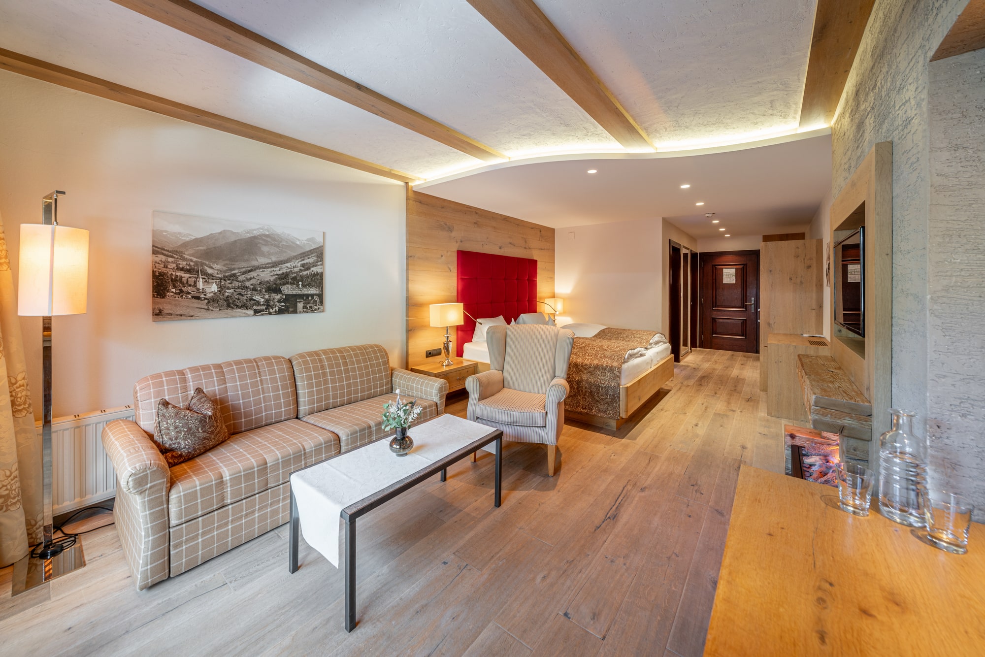 Gemütliches Hotelzimmer mit Holzvertäfelung, einem bequemen Sessel, einem Doppelbett, mit Blick die Zimmertür.