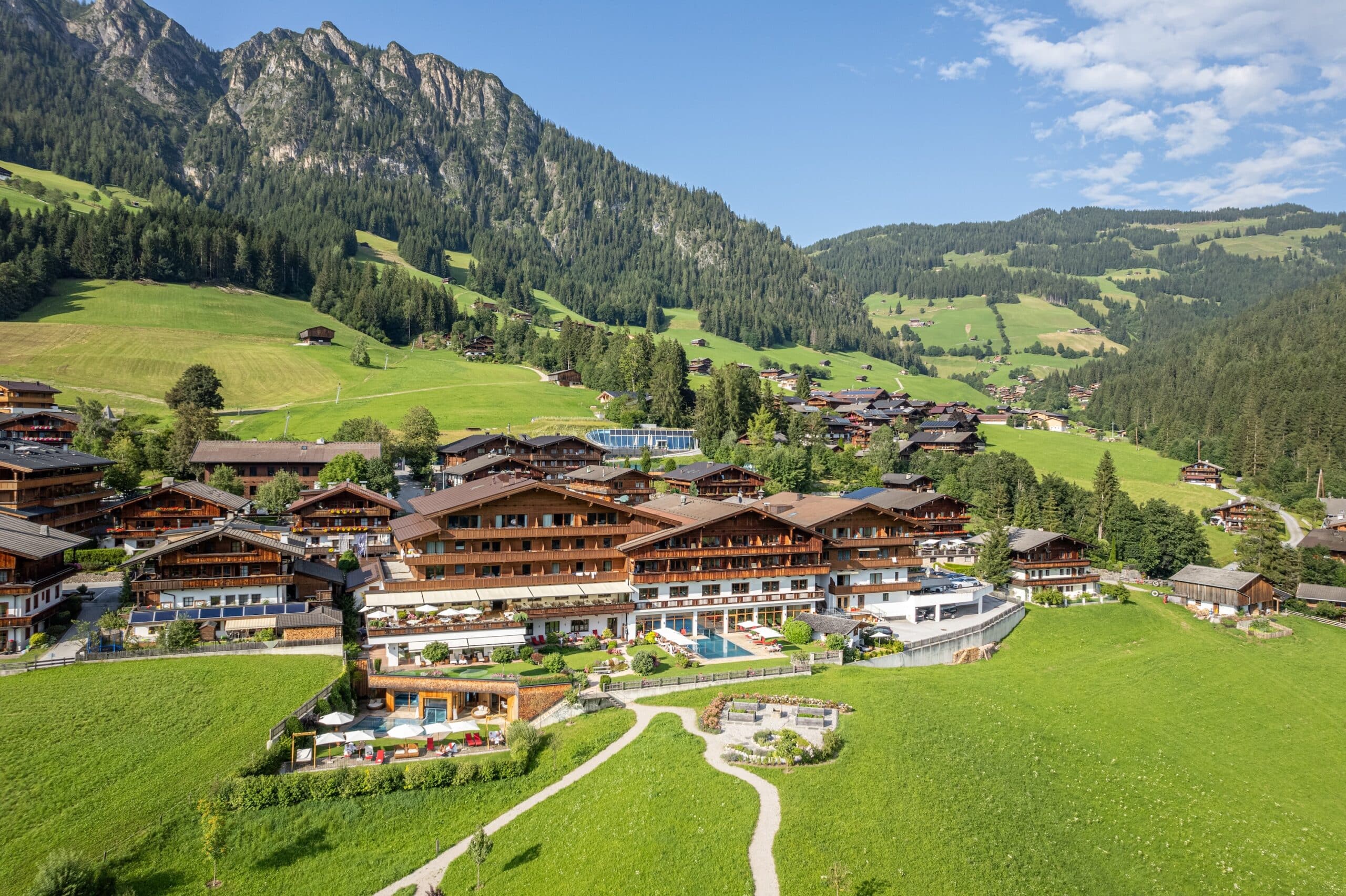 Idyllisches Bergdorf mit traditionellen Holzhäusern, umgeben von grünen Wiesen und einer imposanten Bergkulisse im Hintergrund.