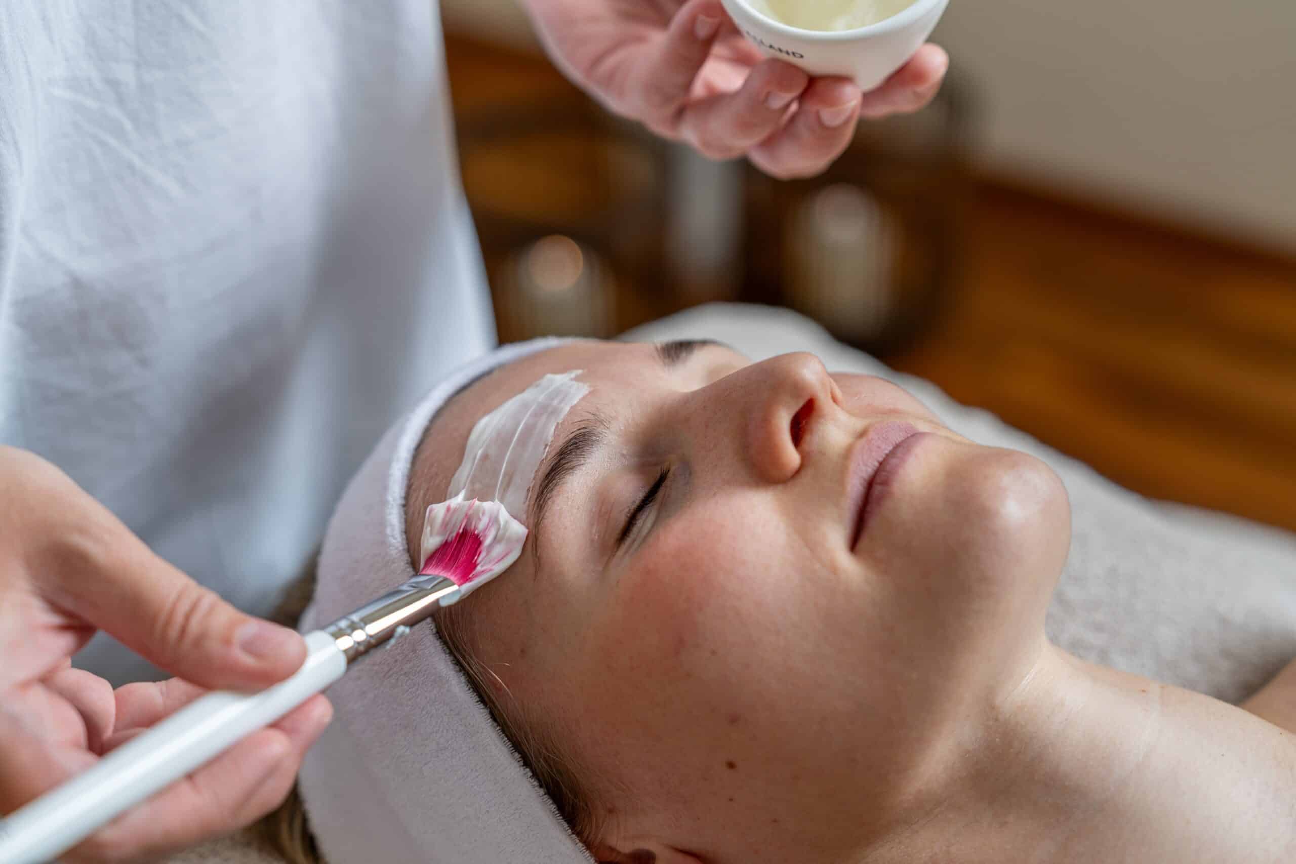 Eine Frau erhält eine entspannende Gesichtsbehandlung, bei der eine Maske mit einem Pinsel aufgetragen wird.