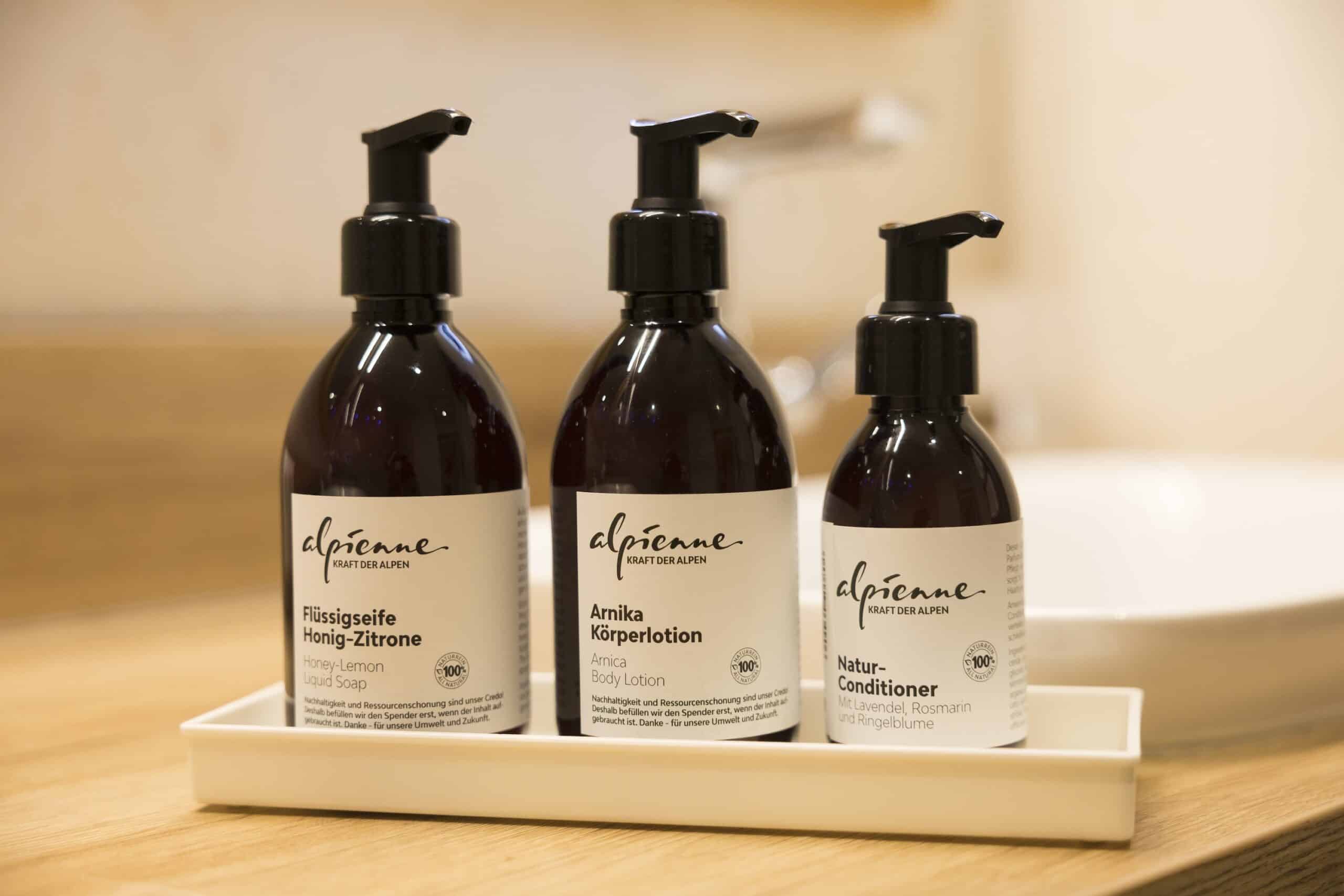 Drei Pumpflaschen mit Naturkosmetikprodukten auf einem weißen Tablett, beschriftet mit „Arnika Honig-Zitrone“, „Körperlotion“ und „Natur-Conditioner“.