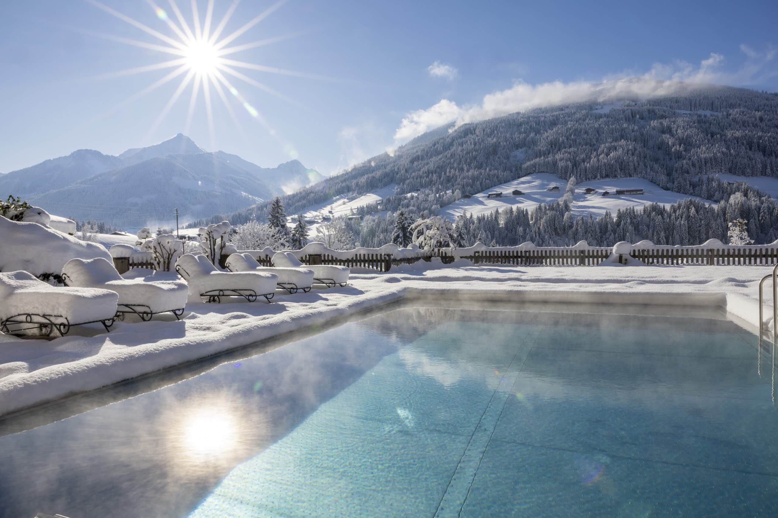 Outdoorpool vor Bergpanorama an einem sonnigen Wintertag