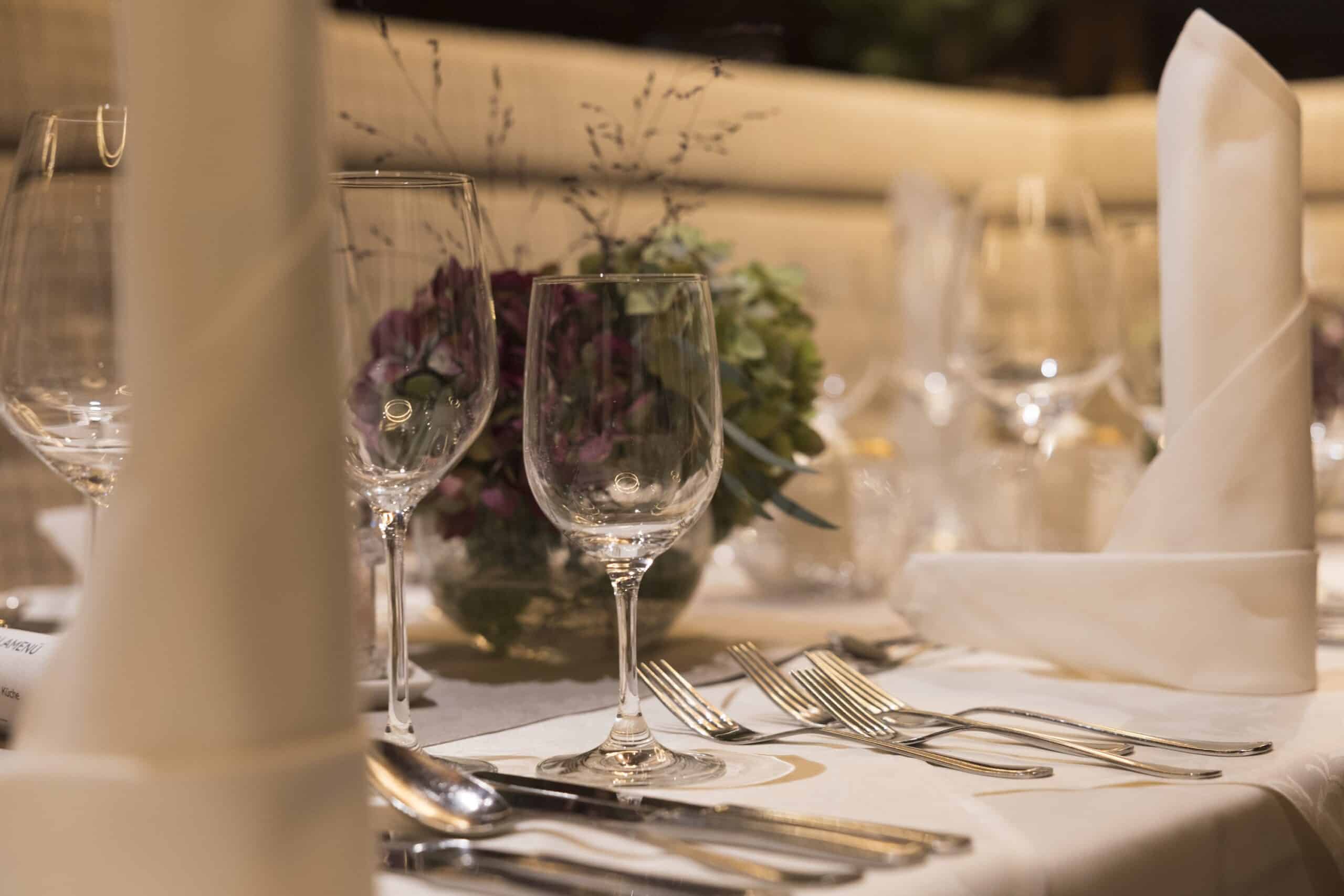 Ein elegant gedeckter Esstisch mit Weingläsern, Besteck und einem Blumenarrangement.