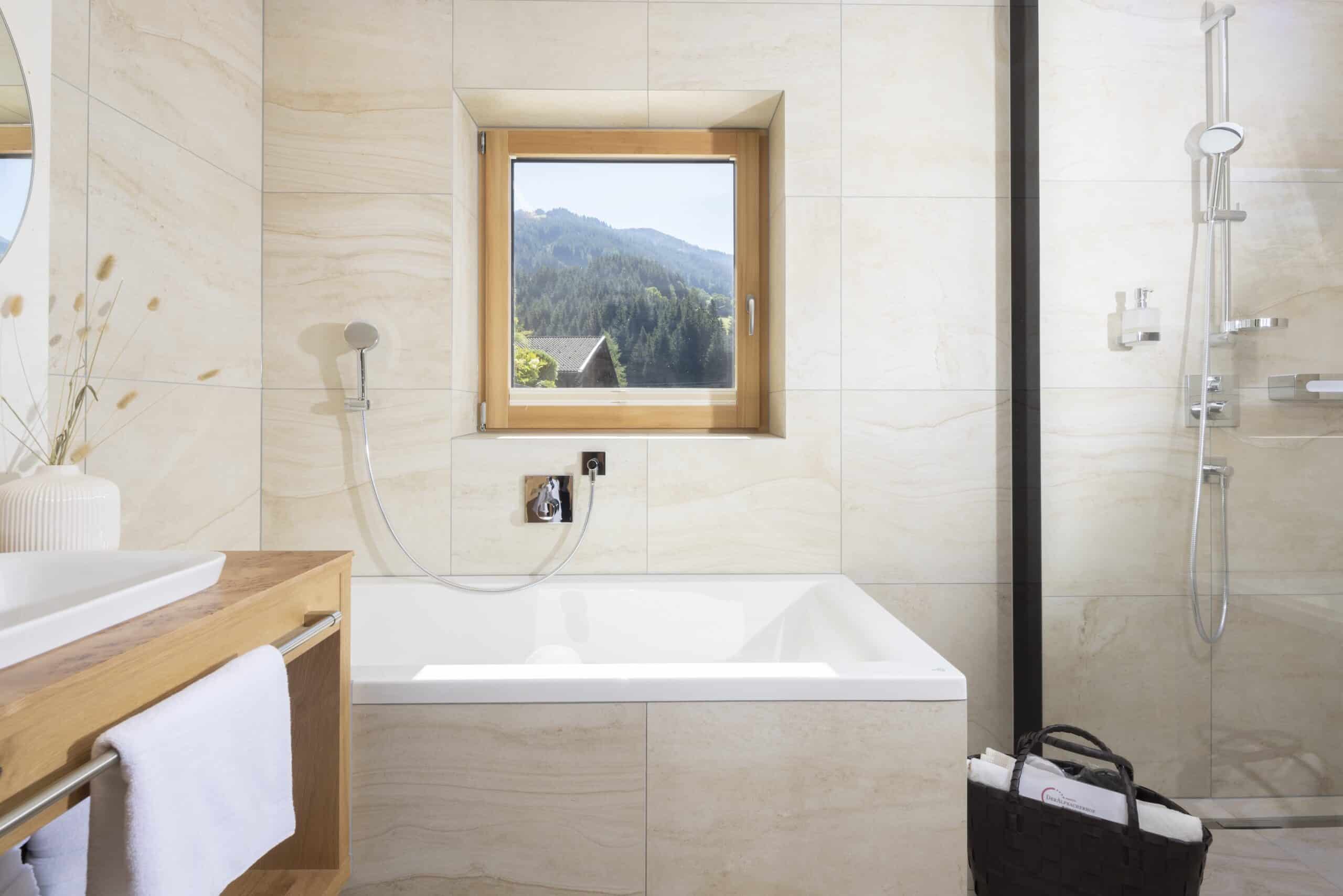 Helles, modernes Badezimmer mit einer Badewanne, einem Waschbecken und einem Fenster mit Blick auf bewaldete Hügel.