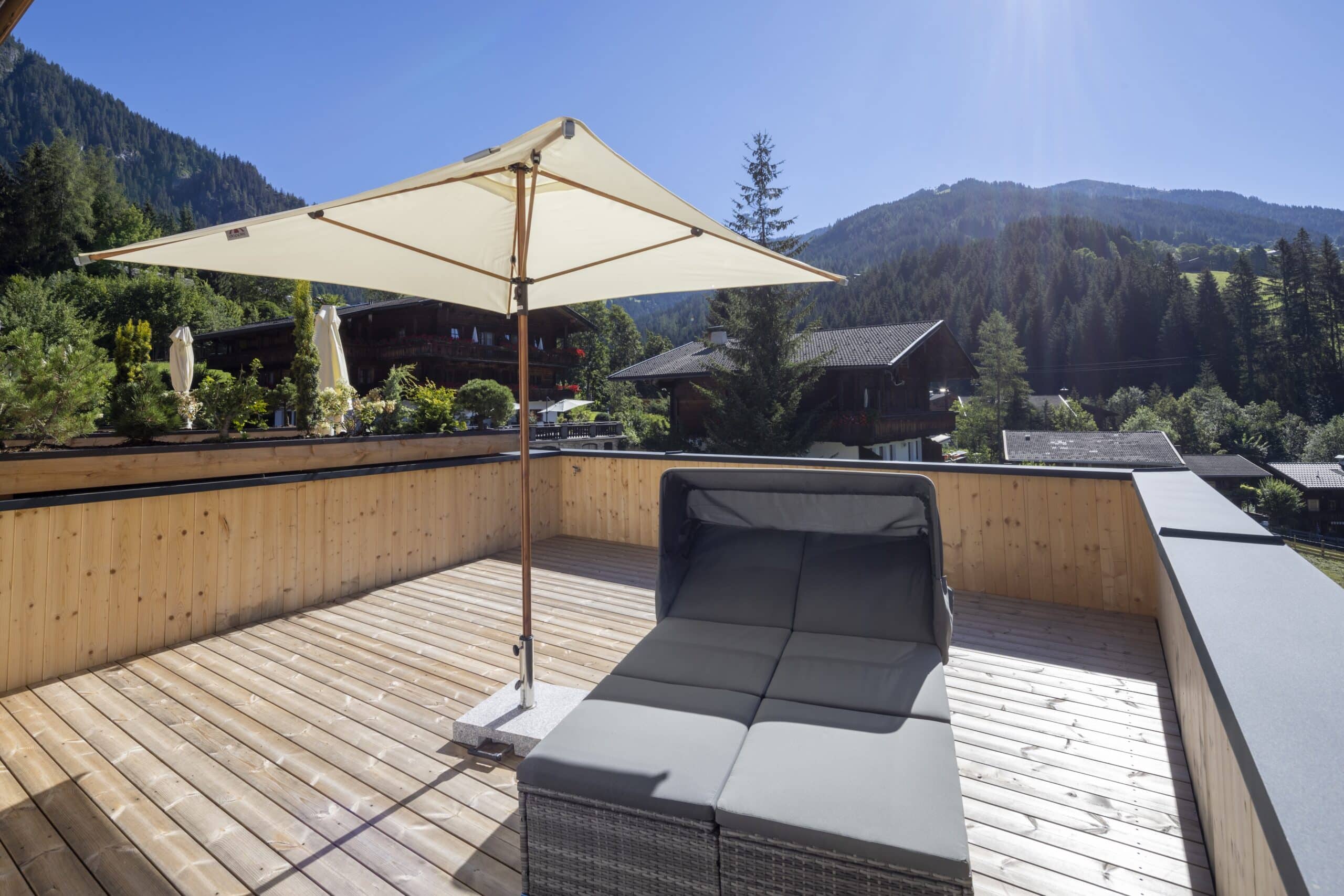 Terrasse mit Liegesofa und Sonnenschirm, mit Blick auf bewaldete Berge in der Ferne.