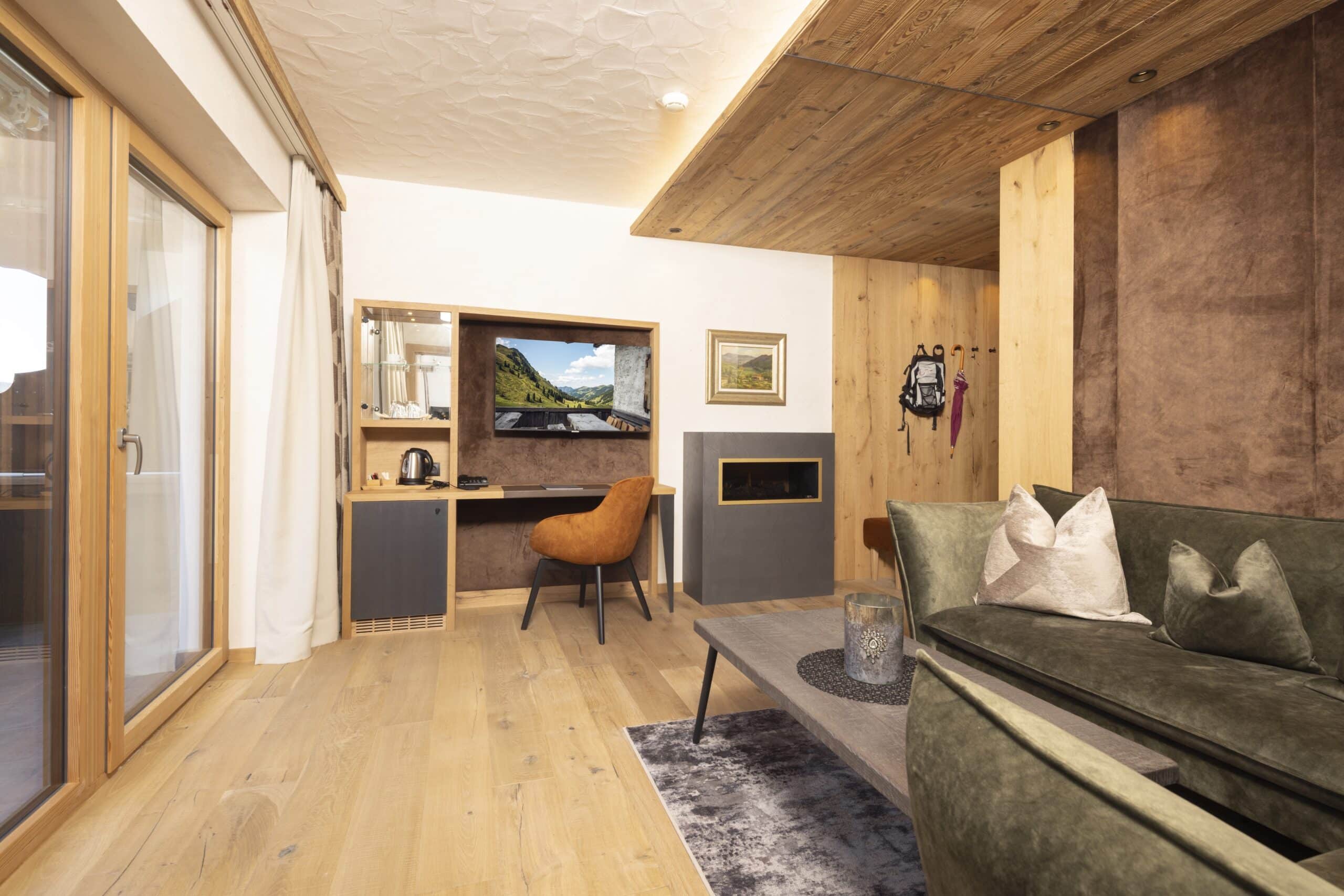 Ein modern eingerichtetes Wohnzimmer mit Holzböden, einer grünen Couch, einem orangen Stuhl und einem an der Wand angebrachten Fernseher, der eine Landschaft zeigt.
