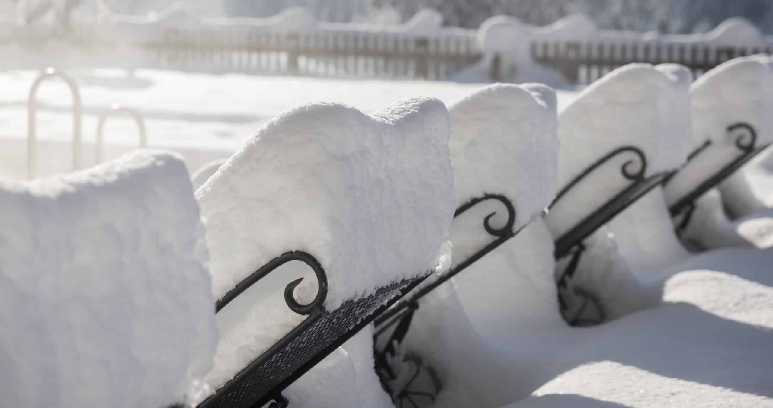Verschneite Parkbank im Sonnenlicht, bedeckt mit einer dicken Schneeschicht.