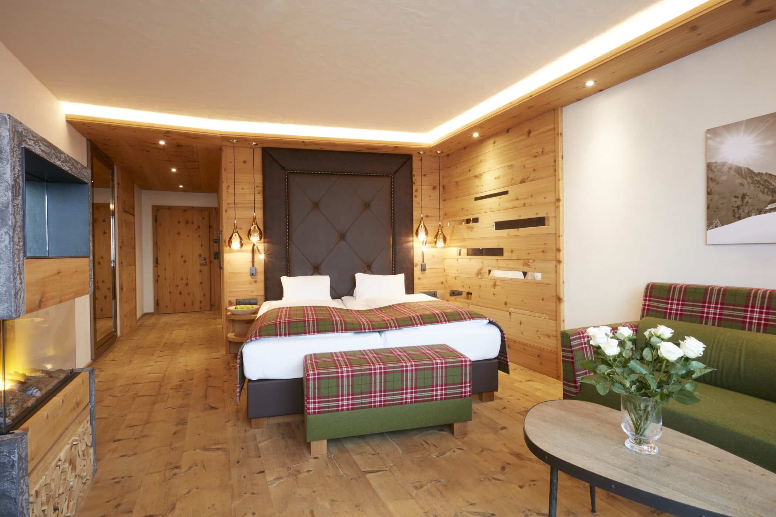 Ein gemütliches, modern eingerichtetes Schlafzimmer mit Holzwänden, einem großen Doppelbett mit kariertem Überwurf und einer Sitzecke mit grünem Sofa und weißen Blumen auf dem Tisch.