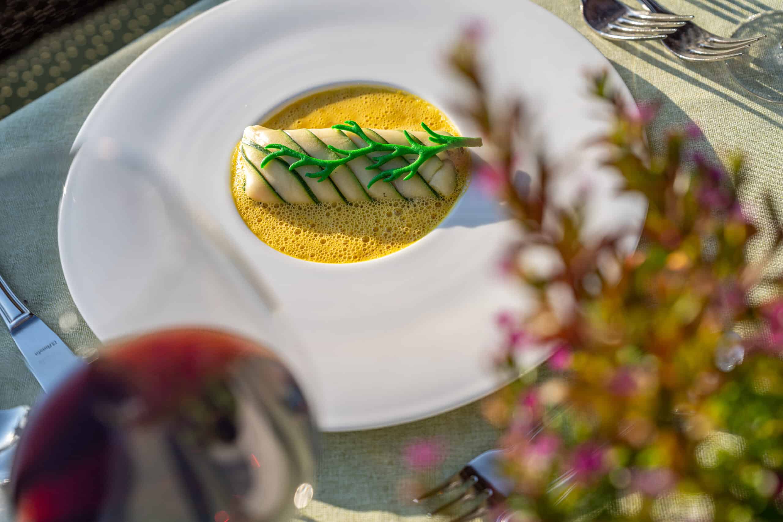 Ein Teller mit einer fein angerichteten Fischfilet auf Safransauce, serviert auf einem elegant gedeckten Tisch im Freien.