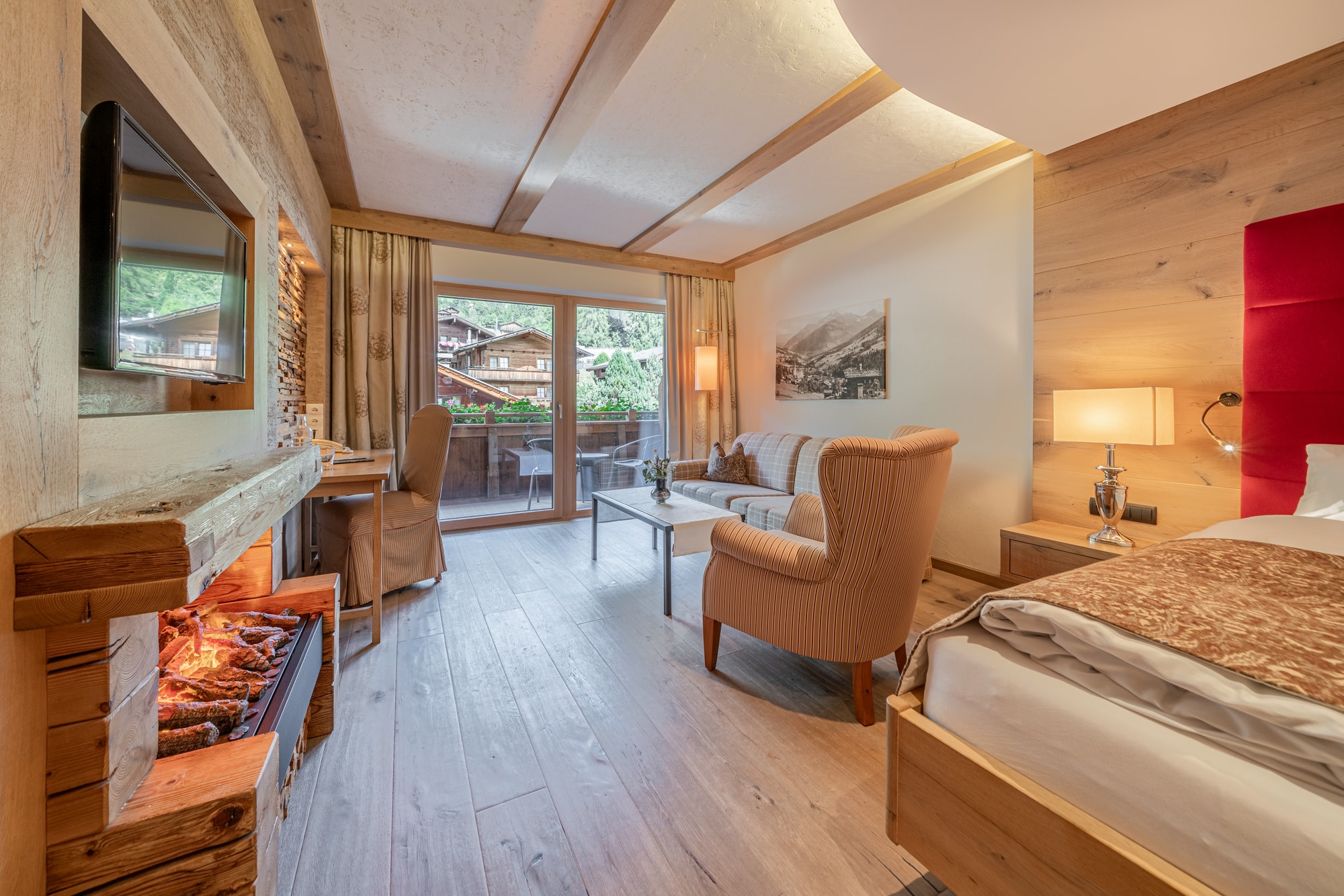 Gemütliches Hotelzimmer mit Holzvertäfelung, einem bequemen Sessel, einem Doppelbett und Kamin, mit Blick auf ein Fenster.