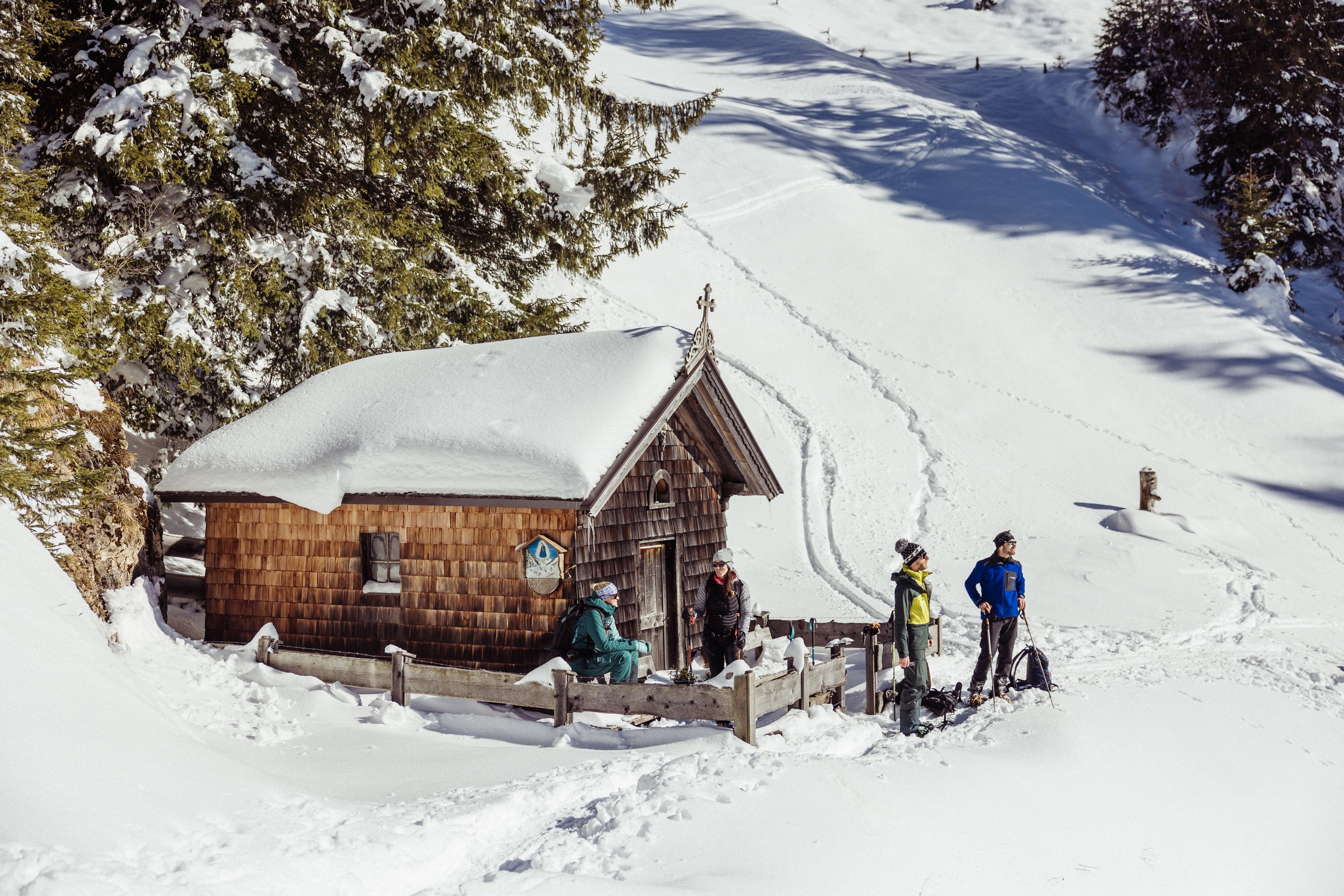 Holzkapelle mit Schindeln, schneebedecktes Dach, Gruppe von Schneeschuhwanderung vor der Kapelle