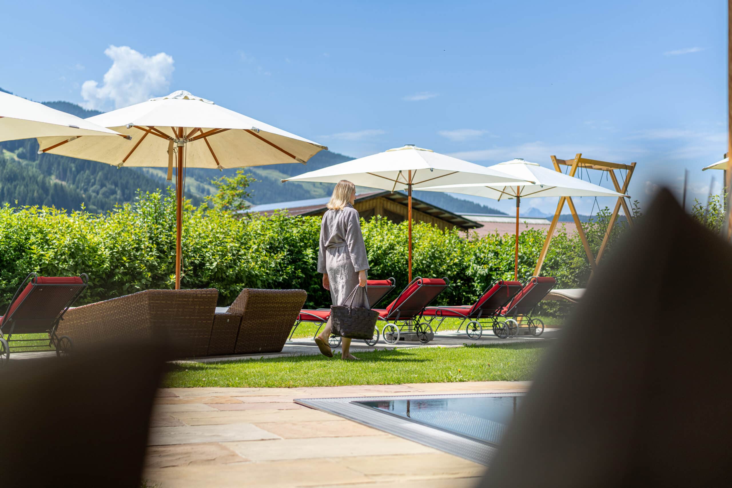 Junge Frau mit Wellnesstasche am Pool mit Blick in die grüne Natur