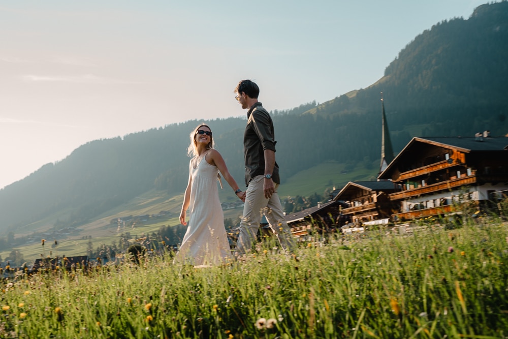 Pärchen spaziert hand in hand durch wiese, Hintergrund Häuser und Kirchturm