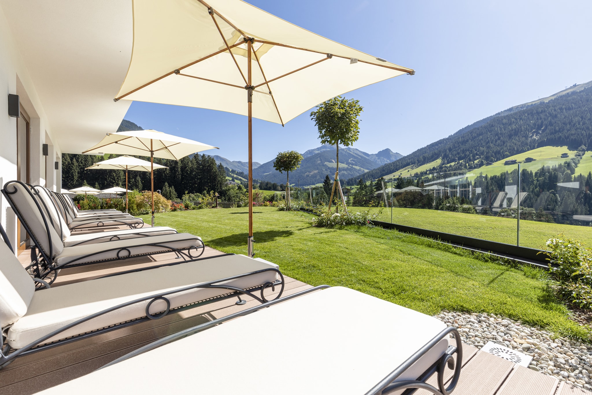weiße Relaxliegen im Freien mit blick in die Natur, grünes Gras, Grasberge, blauer himmel, weißer Sonnenschirm